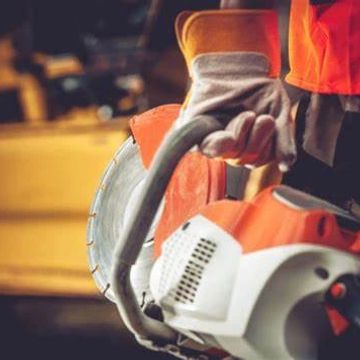 Worker holding a power saw, wearing protective gloves.