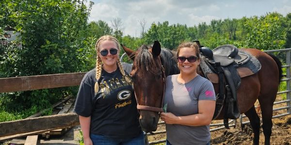 Two women smiling with a brown horse.