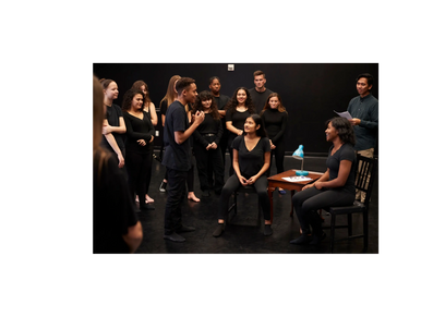 A diverse group rehearses a scene in a theater studio.