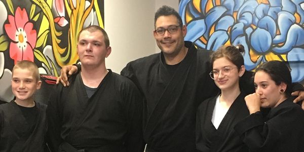 A group of five people in black martial arts uniforms posing indoors.