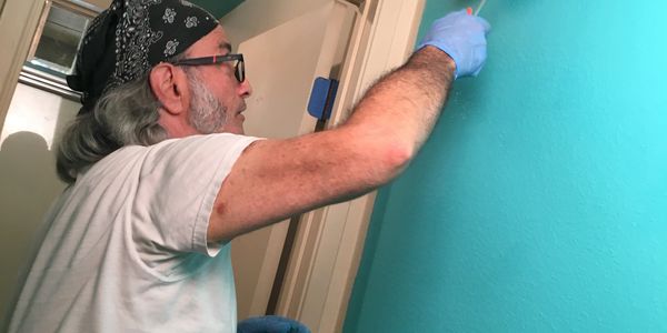 Man painting a wall turquoise with a roller brush indoors.