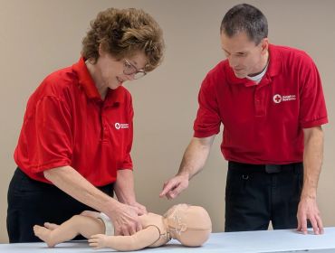 Two people practicing CPR on an infant mannequin.
