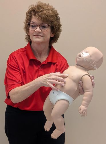 Woman demonstrating infant CPR on a training mannequin.