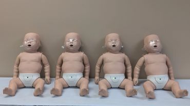 Four baby CPR mannequins lined up on a table.