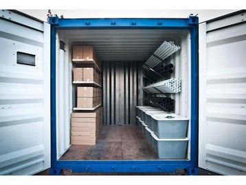 Organized storage inside a shipping container with boxes and pipes.