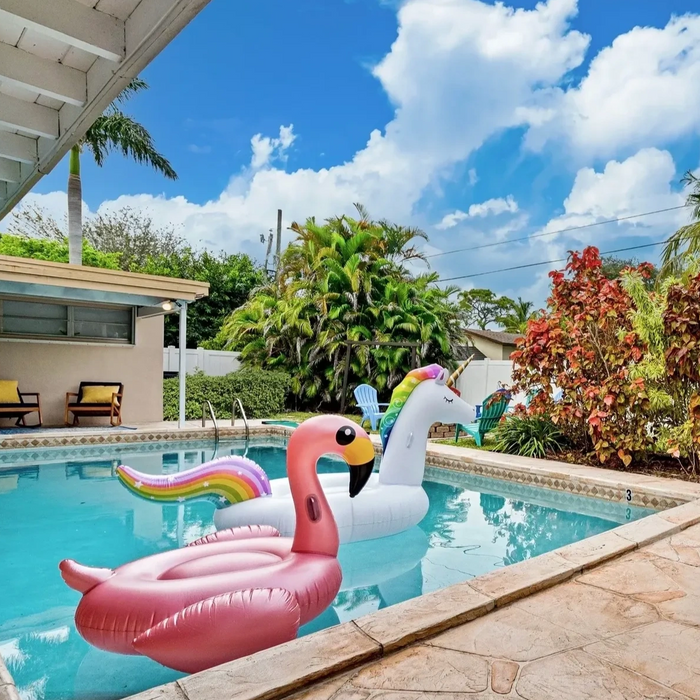 A sunny backyard pool with colorful inflatable unicorn and flamingo floats.