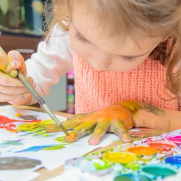 Child painting their hand with watercolors for art.
