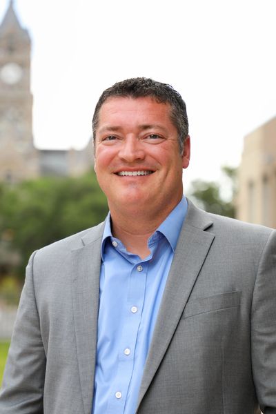 Smiling man in a gray suit and blue shirt outdoors.