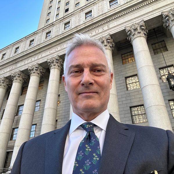 Man in suit taking selfie outside a grand courthouse building.