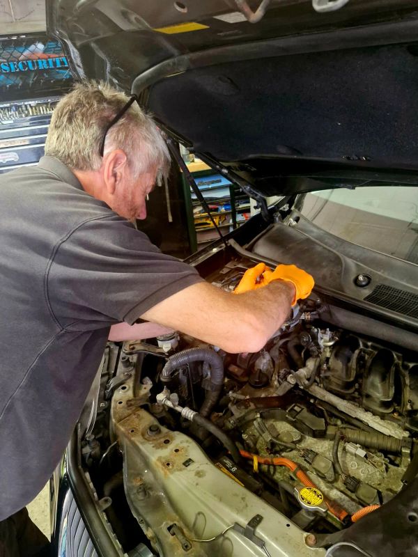 A man wearing orange gloves repairs a car engine in a garage.