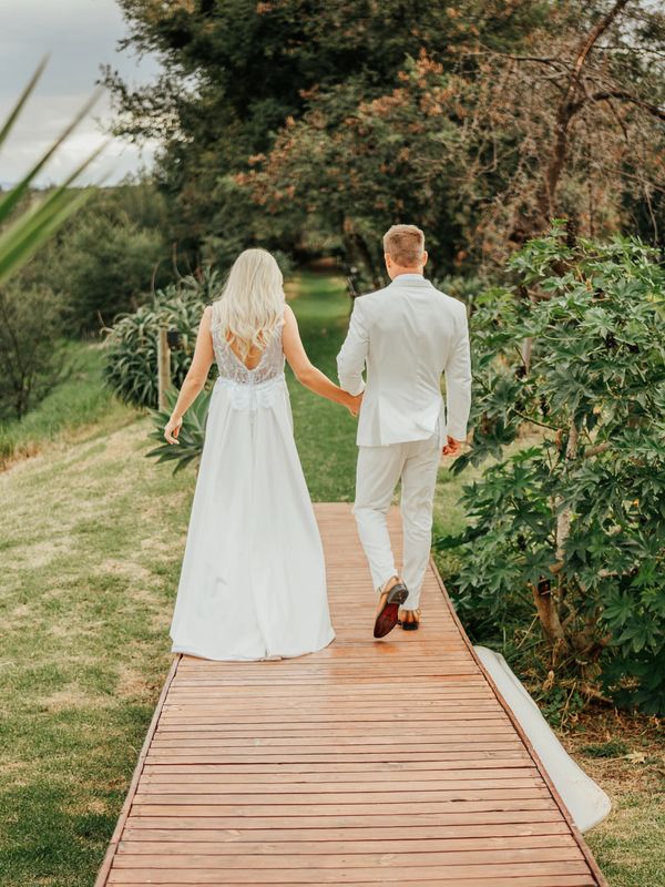Bride and groom holding hands walking on a wooden path outdoors.