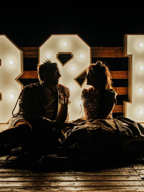 Silhouetted couple in vintage attire backlit by illuminated letters at night.