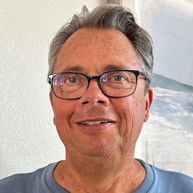 Smiling middle-aged man wearing glasses and a blue shirt.