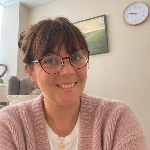 Smiling woman with glasses in cozy indoor setting.