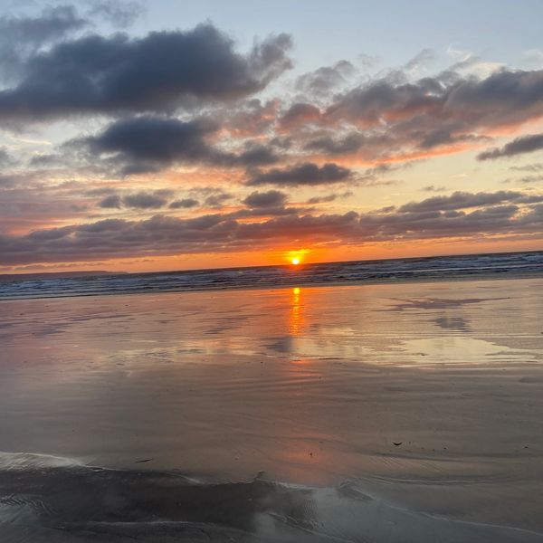 Sunset over a calm beach with reflected clouds.