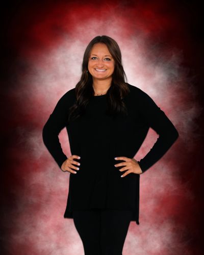 Woman smiling with hands on hips against red smoky background.