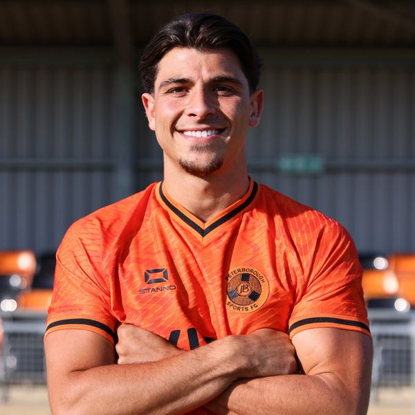 Smiling football player in orange Peterborough Sports FC jersey.