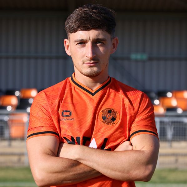 Young man in Peterborough Sports FC jersey with arms crossed.