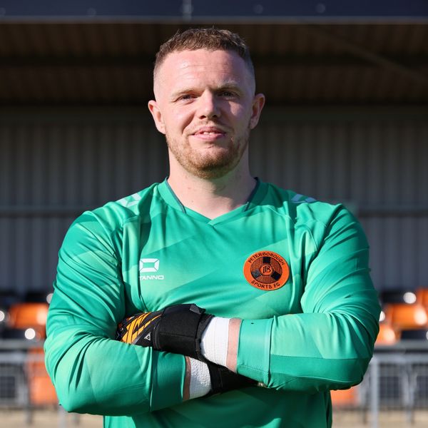 Football goalkeeper in green jersey with crossed arms.