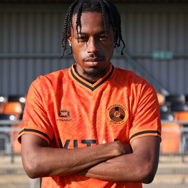 Man in orange Peterborough Sports FC jersey with arms crossed.