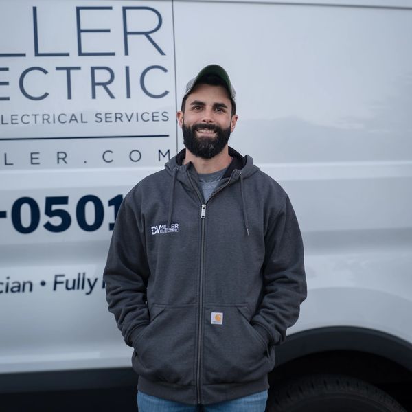 Photo of Darry Miller smiling and standing in front of a D.V. Miller Electric work van with his hand