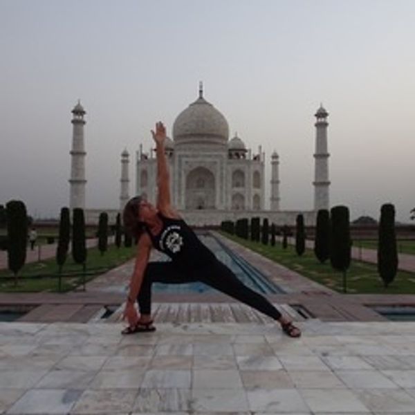 Person practicing yoga in front of the Taj Mahal at dawn.