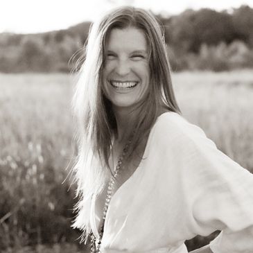 A woman with long hair smiles joyfully in a sunlit field.