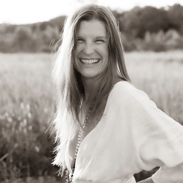 A woman with long hair smiles joyfully in a sunlit field.