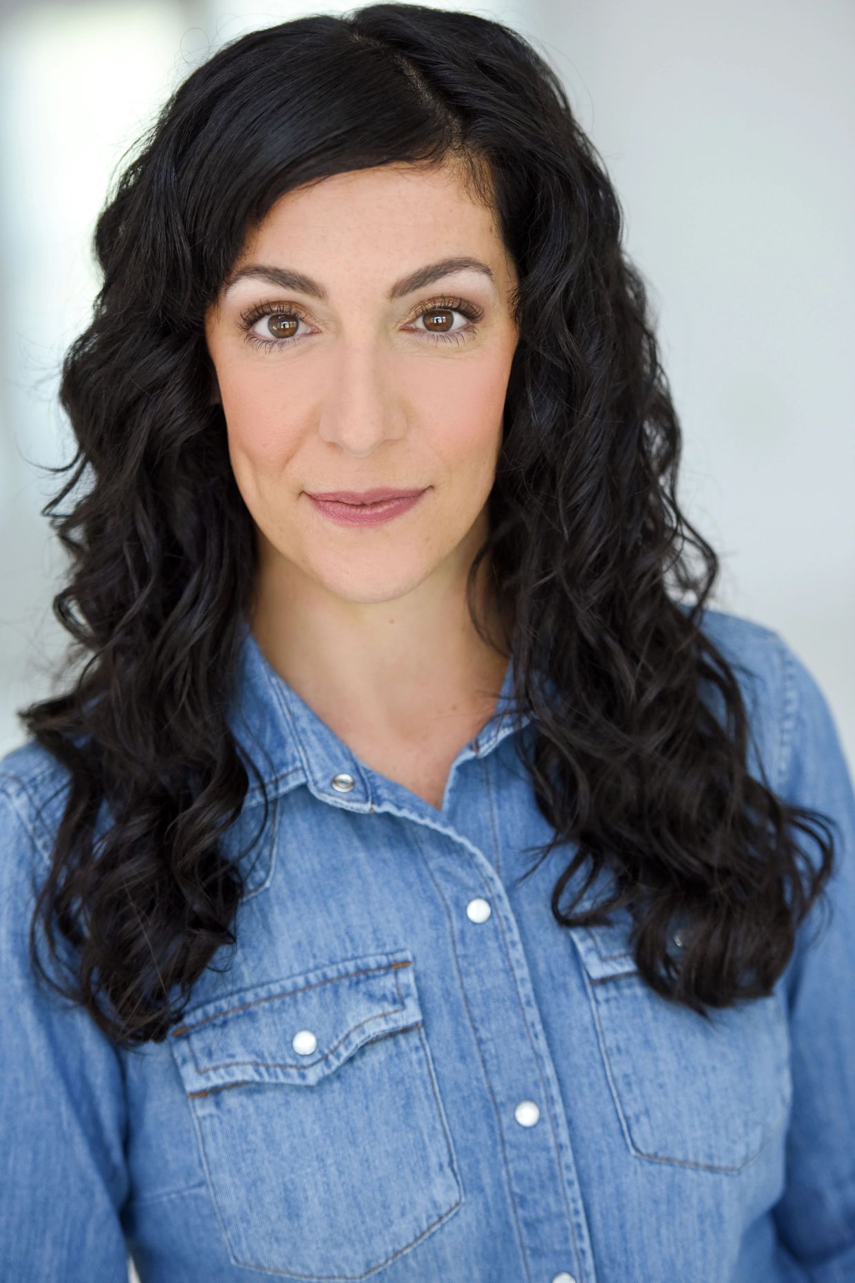 Woman with curly dark hair in a denim shirt.