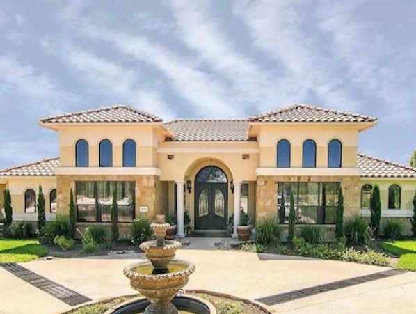 Elegant Mediterranean-style villa with a clay tile roof, arched doorways, and a grand entrance, framed by lush landscaping.