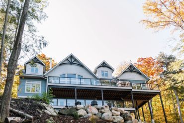 Lake side view of the cottage with two sprawling decks overlooking the lake and firepit. 