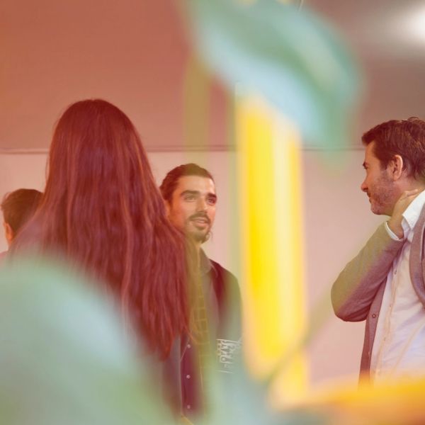 Coloured imaged of three individuals chatting with others in the background, some in business attire 