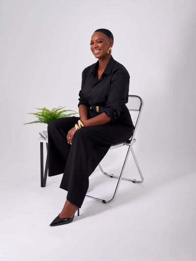 Woman in black outfit sitting on a chair and smiling.