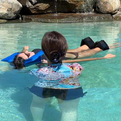 Two people relaxing in a clear pool with rocks and a waterfall in the background.