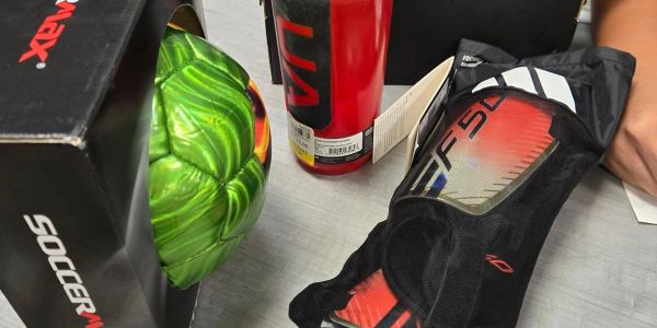 Green soccer ball, red bottle, and black knee or elbow pads on table.