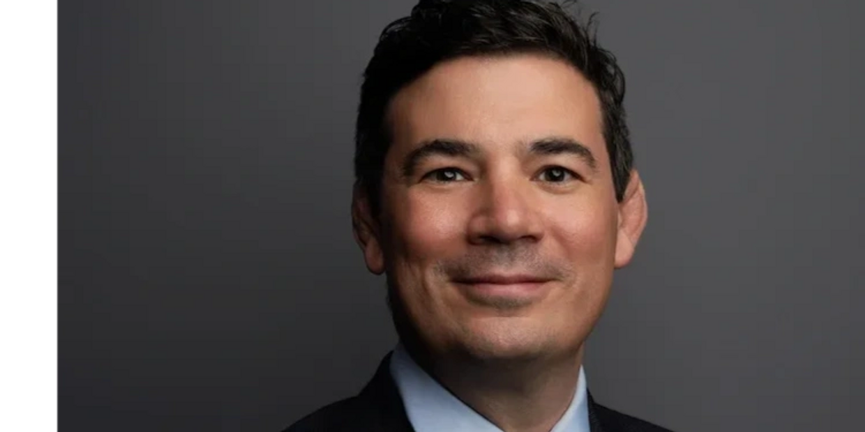 Professional man in suit with a confident smile against a gray background.