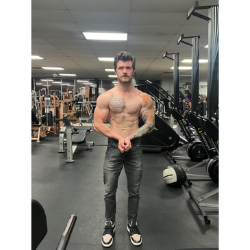 Muscular man with tattoos posing shirtless in a gym.