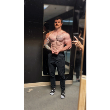 Muscular man with tattoos posing shirtless in front of a mirror.