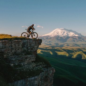 Fahrradfahrer auf Felskante mit Berg im Hintergrund.