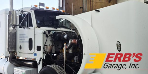 Large white truck with exposed engine being serviced in a garage.