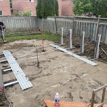 Backyard under construction with dirt, metal beams, and wooden fence.