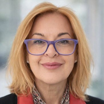Smiling woman with blonde hair and purple glasses in a professional setting.
