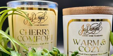 Two luxury scented candles labeled Cherry Comfort and Warm & Cozy with green succulent plants.