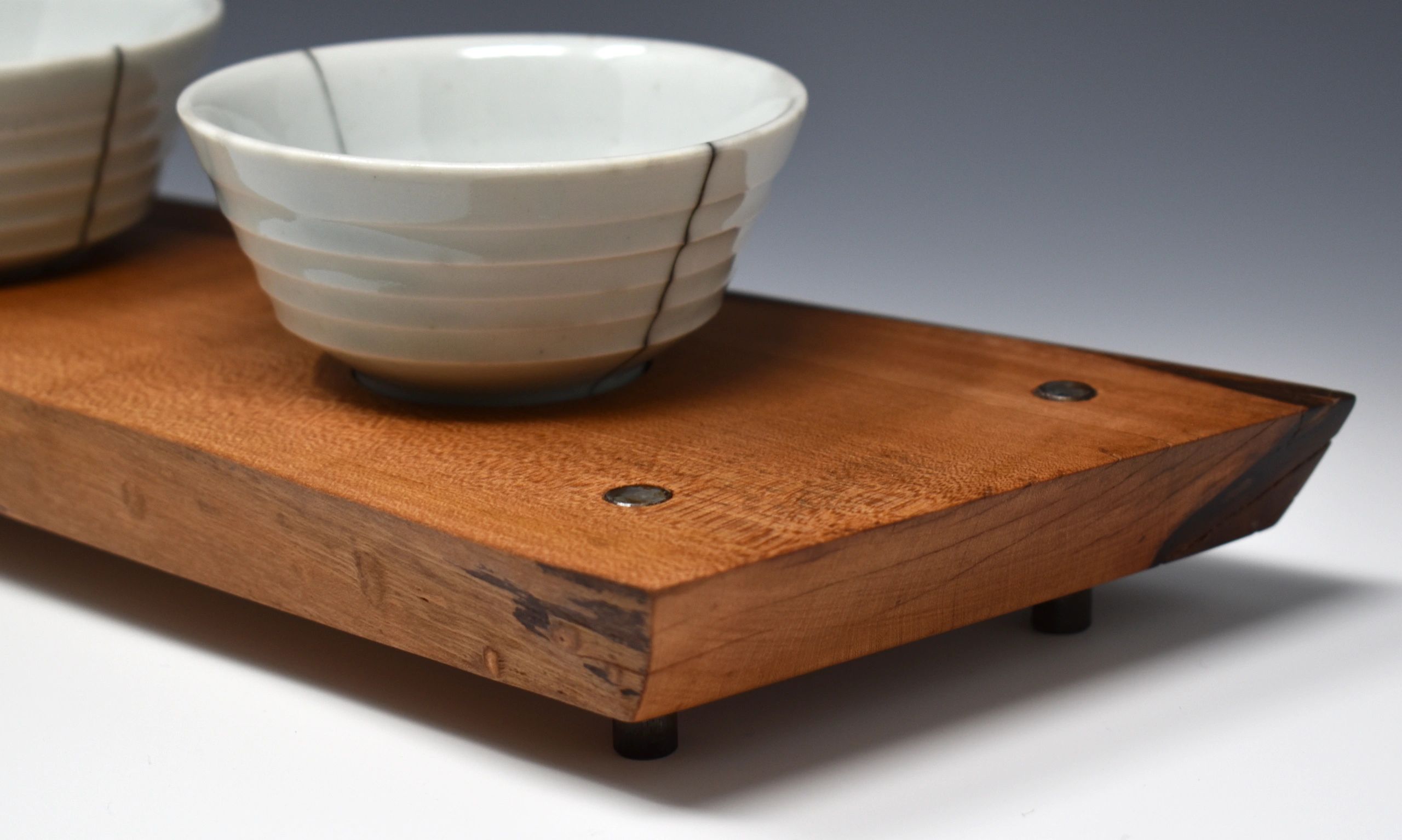 Detail image of the corner of a wood tray with two porcelain copitas resting on it. 