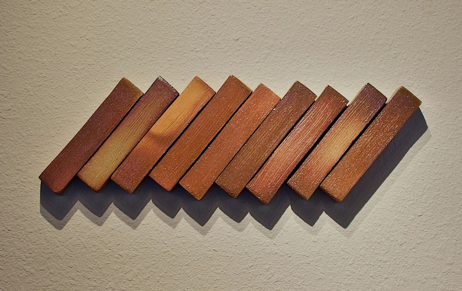 Nine soda fired stoneware rectangular forms installed at slight slant on the wall casting a shadow