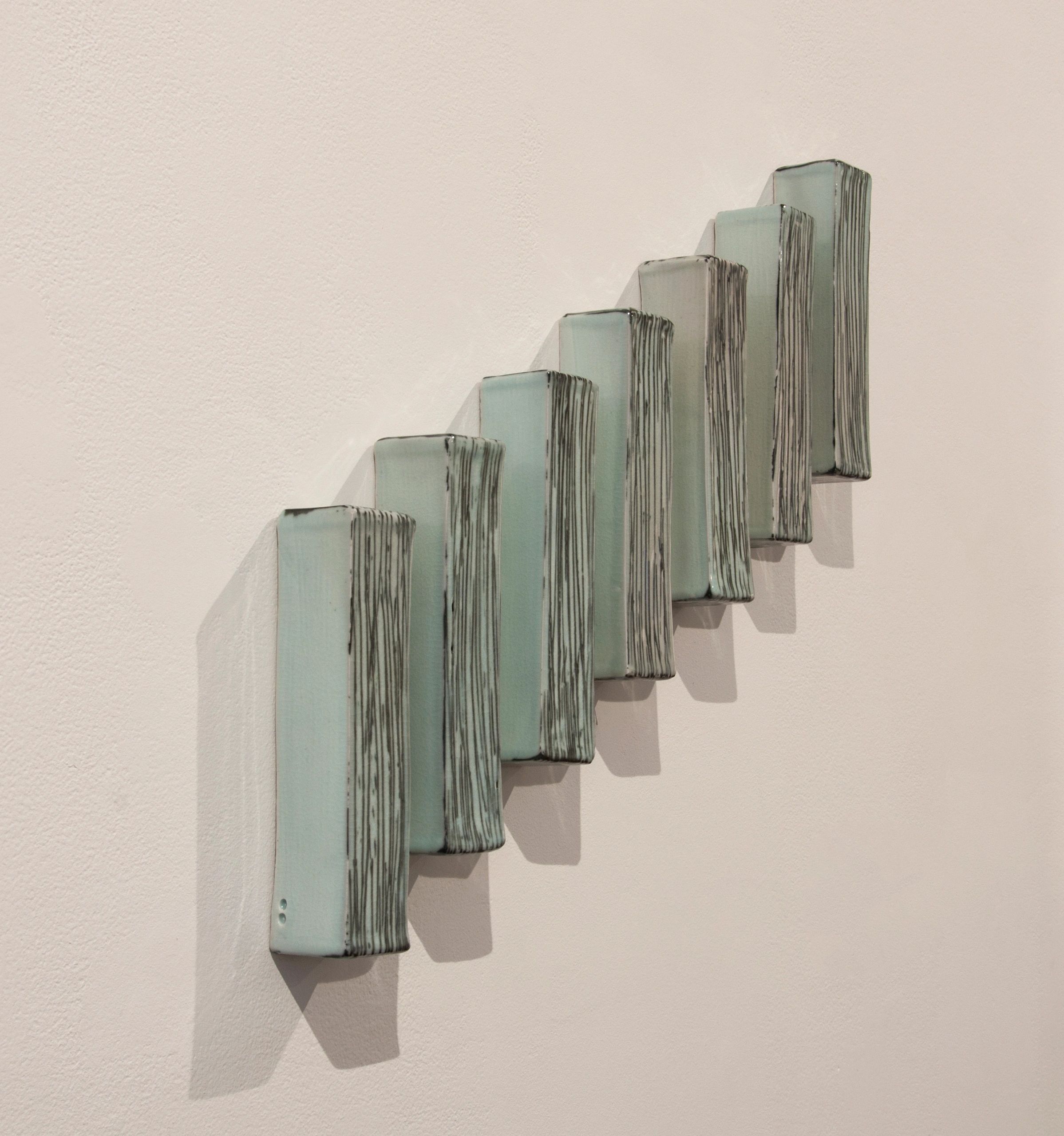 Seven porcelain rectangular forms installed on the wall using the shadows as part of the composition