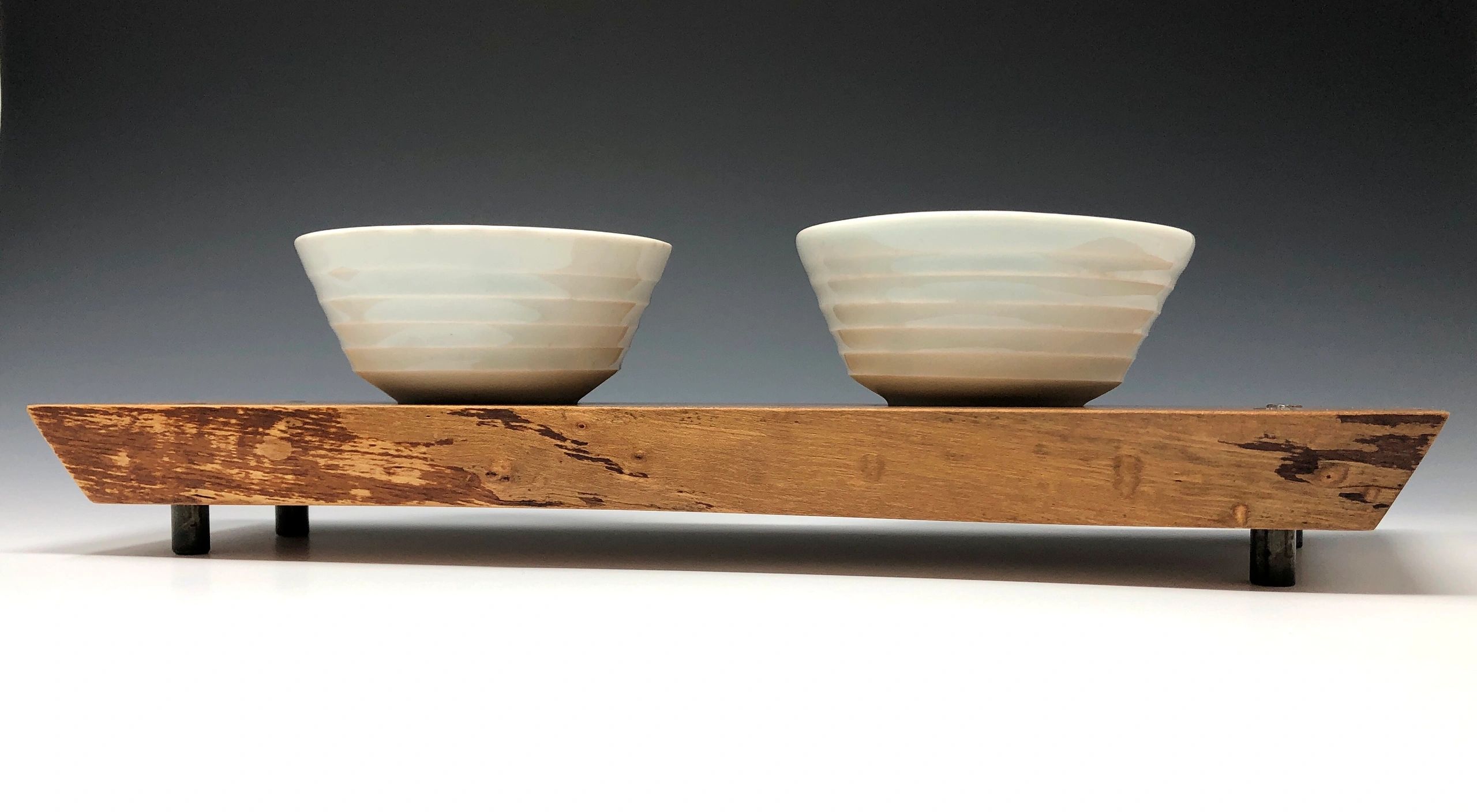 two porcelain copitas sitting on a finished wood tray.  The four short legs of the tray are steel.  