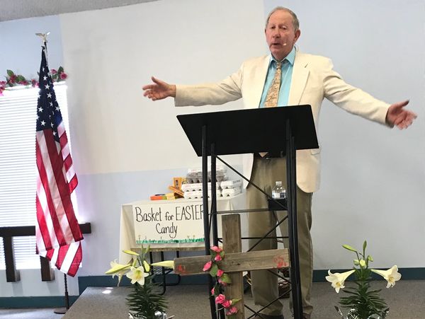 Pastor behind podium on small stage preaching to church