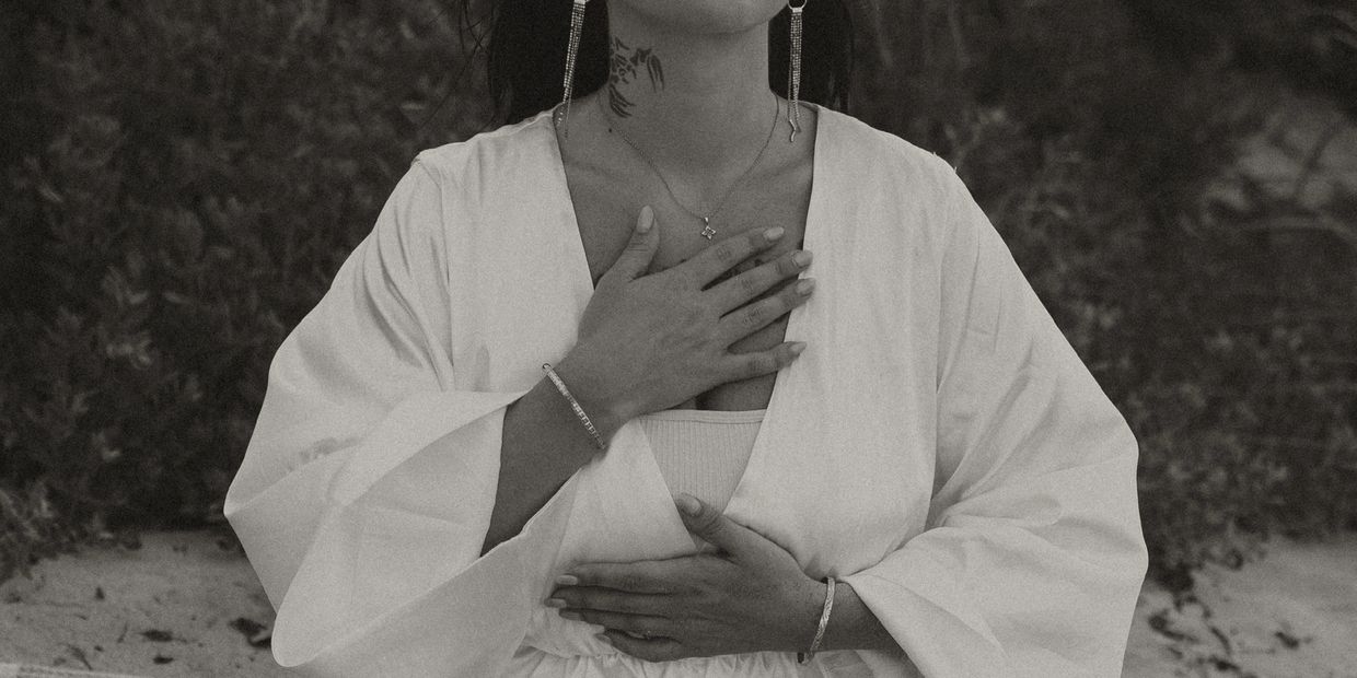 Woman in white robe with hands on chest and stomach in a calm pose.