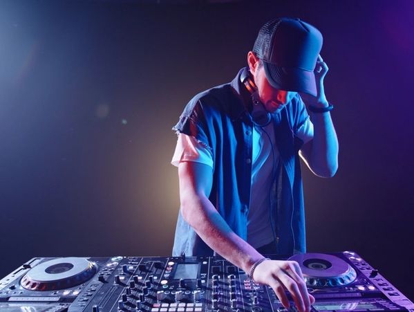 Cool hipster disc jockey performing in a nightclub at a mixer controller